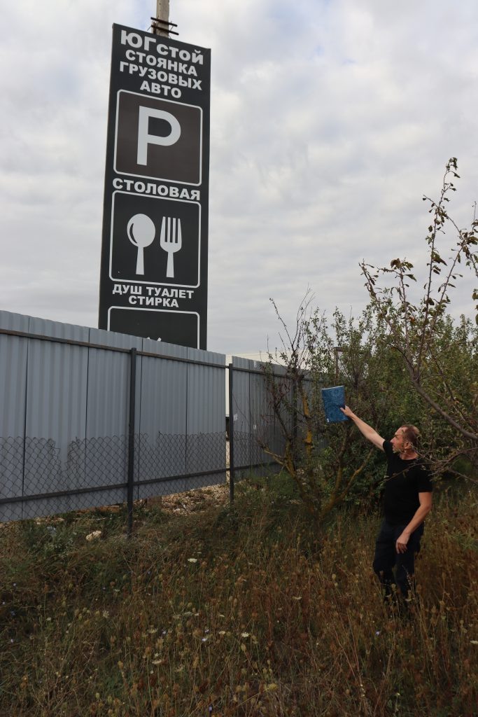    Иначе как издевкой эту вывеску не назовешь. Ее закрепили вплотную к изгороди, обернув лицевой стороной к домохозяйству соседей. То есть получается: это у Круковелов — столовая, душ, туалет, стирка. Ну и стоянка грузового транспорта, само собой.