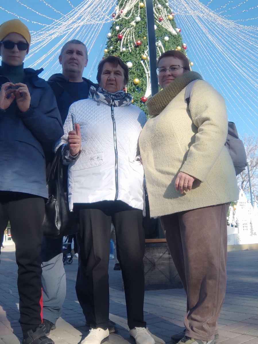 Тифлокомментарий. Это мы в прошлом году в Геленджике на Новый год. Фото в полный рост: Гоша, муж, свекровь и я. Позади новогодняя ёлка. 