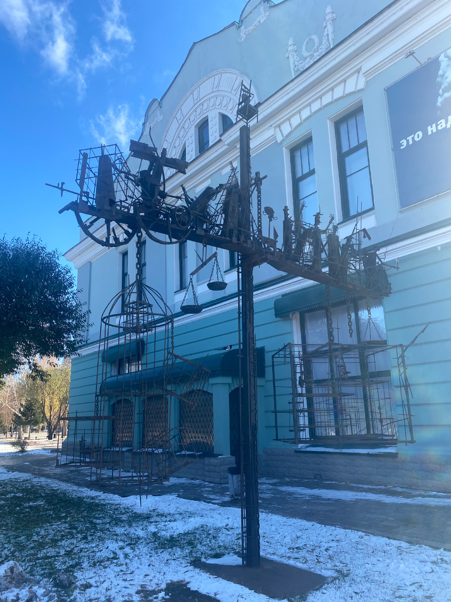 Скульптура «Динамическое равновесие, или весы бытия» слева рядом с музеем. 