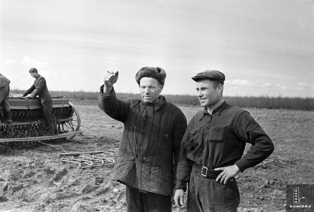 Бригадир колхоза имени И.В. Сталина Слуцкого района К.Н. Кощаев и его сын тракторист М.К. Кощаев на поле перед севом, на заднем плане — отец и сын Семен и Сергей Карпиевичи — засыпают зерно в сеялку, Минская область, апрель 1961 г.