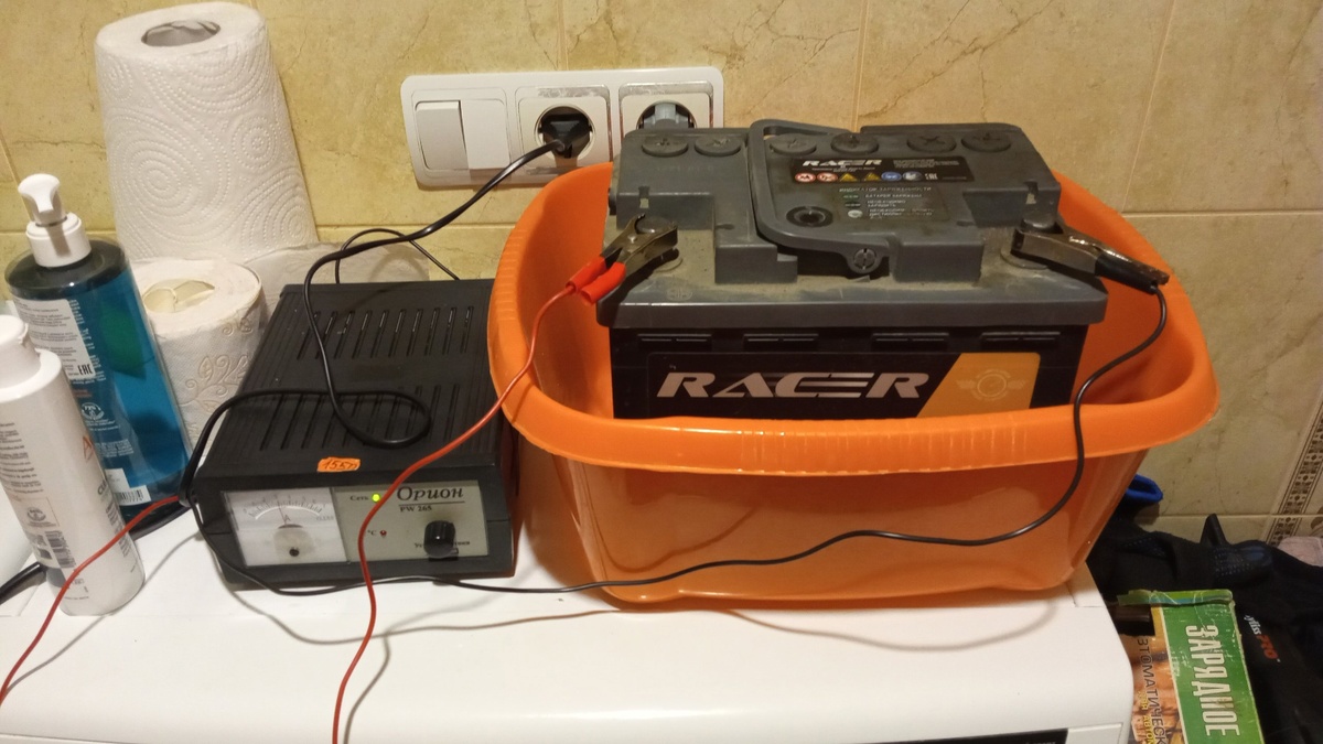 Слева - зарядное устройство. Справа - аккумулятор в тазике. Еще правее инструкция на зарядное устройство.