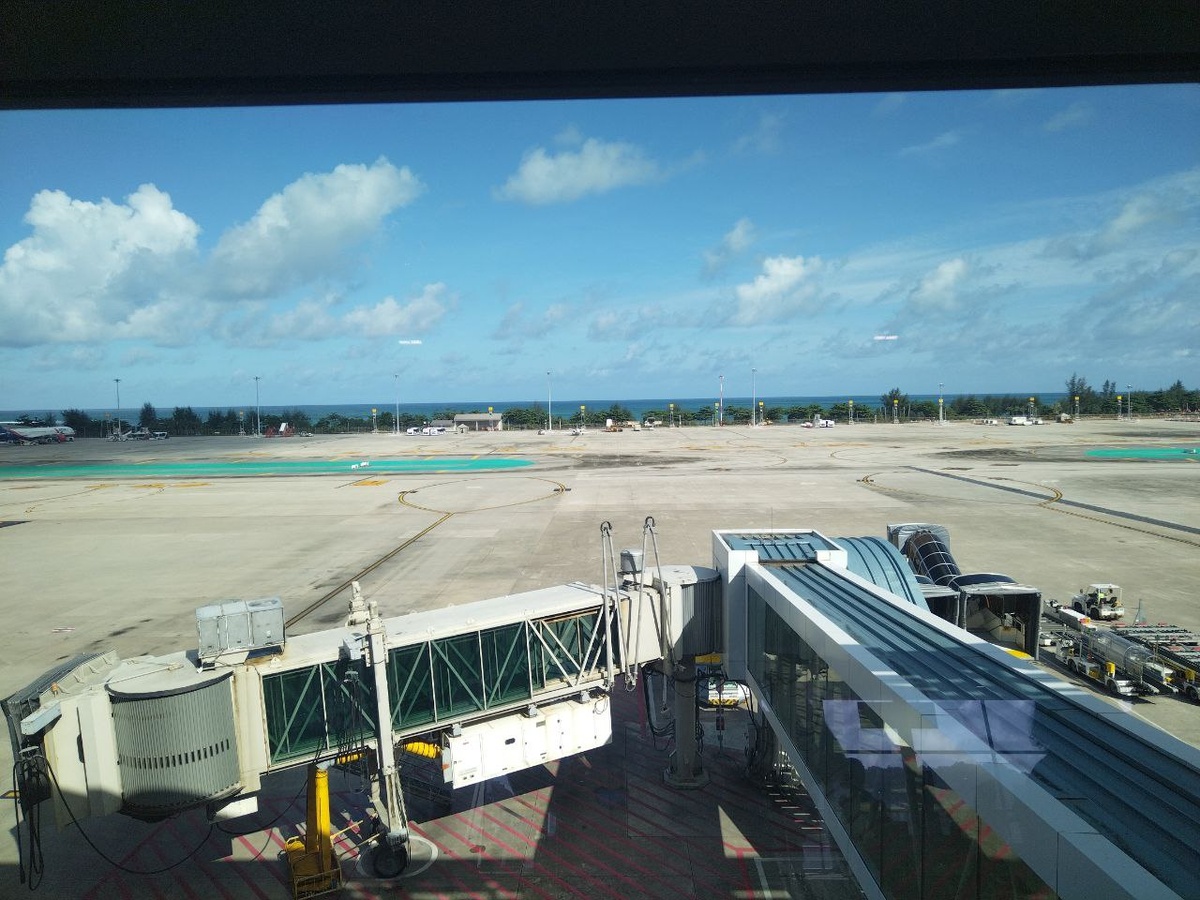 Это довольно эффектный вид из "чистой зоны" аэропорта острова Пхукет — он стоит прямо на берегу Андаманского моря! На переднем плане лётное поле и телетрап, позволяющий провести быструю посадку в самолёт.