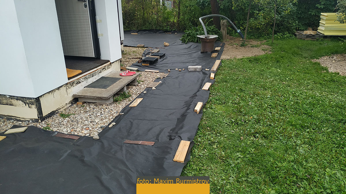 Геотекстиль постелен поверх утрамбованного песка, но далеко на старую гравийную отмостку он не заходит, это не нужно.