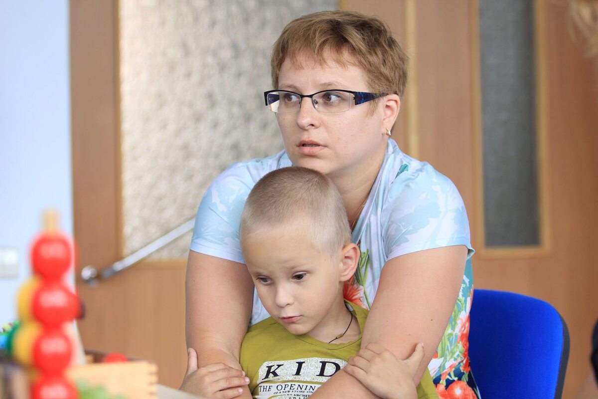 Тифлокомментарий. На фото я и пятилетний Гоша. Первый день на проекте, знакомство со специалистами. Я до сих пор без боли не могу смотреть на это фото. Я сижу на стуле, Гоша стоит на полу, я руками, как крыльями, закрываю его. Гоша держит меня за руки. 