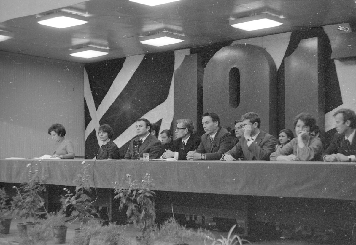 На переднем планом за столом президиума сидят слева направо: 1. … 2. … 3. Кузнецов Юрий Гаврилович – директор РИЗа. 4. Мишин Вадим Георгиевич – заместитель секретаря парткома РИЗа. 5. Гайфуллин Загит Зиннатулович – председатель профкома РИЗа. 6. Кулаков Николай Иванович – секретарь комитета комсомола РИЗа. 7. … 8. …