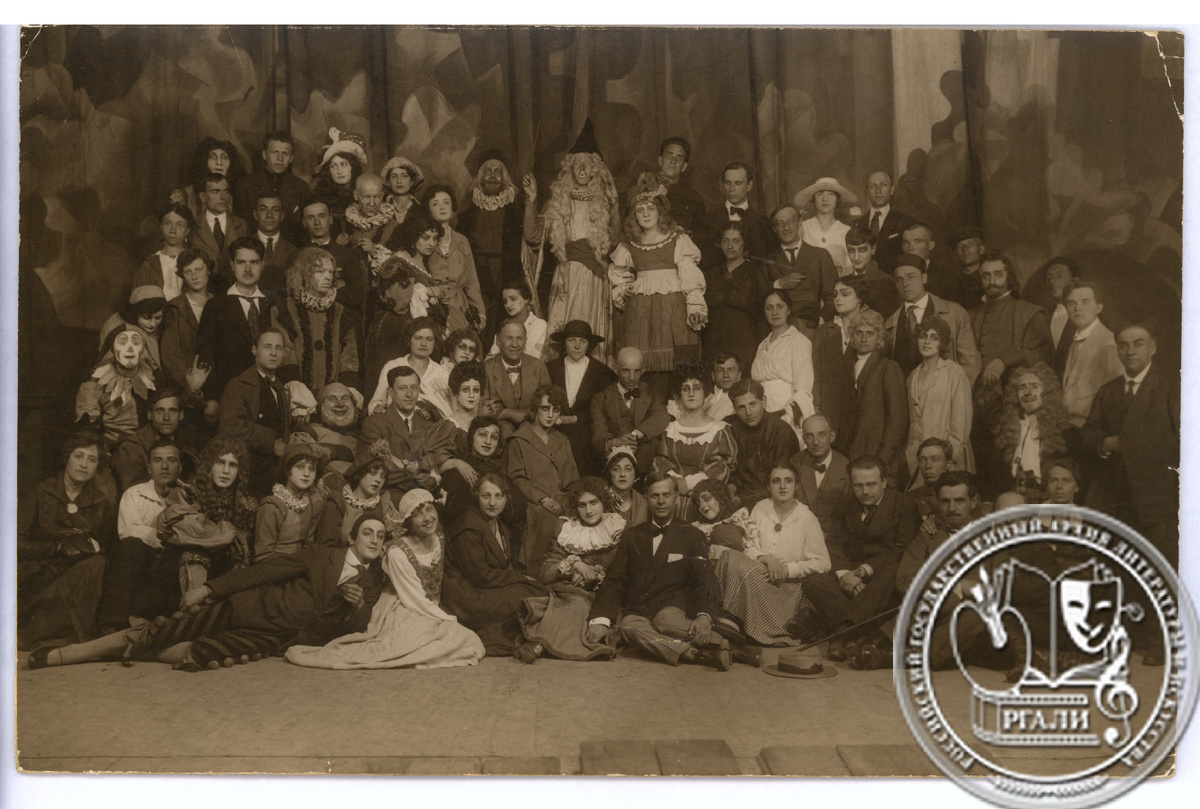 Фотография участников спектакля Театра-студии ХПСРО «Виндзорские проказницы», учащихся и руководителей студии. (М.И. Жаров в роли шута первый слева с поднятой рукой; среди присутствующих в центре Ф.Ф. Комиссаржевский и Е.К. Малиновская). [1919–1920 гг.] РГАЛИ. Ф. 3061. Оп. 1.