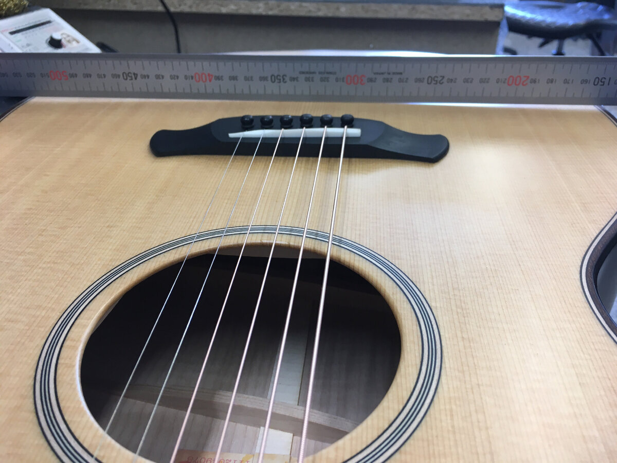 С завода, верхняя дека гитары, за бриджем обычно слегка выпирает.