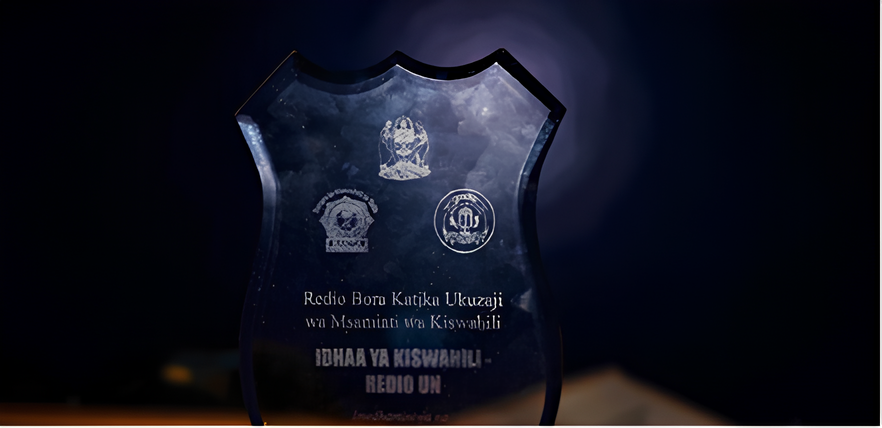 На щите написано: «Лучшее радио по развитию словаря суахили. Программа передач на суахили. Радио ООН».Фото из Habari za UN. 20 Januari 2021 Utamaduni na Elimu
