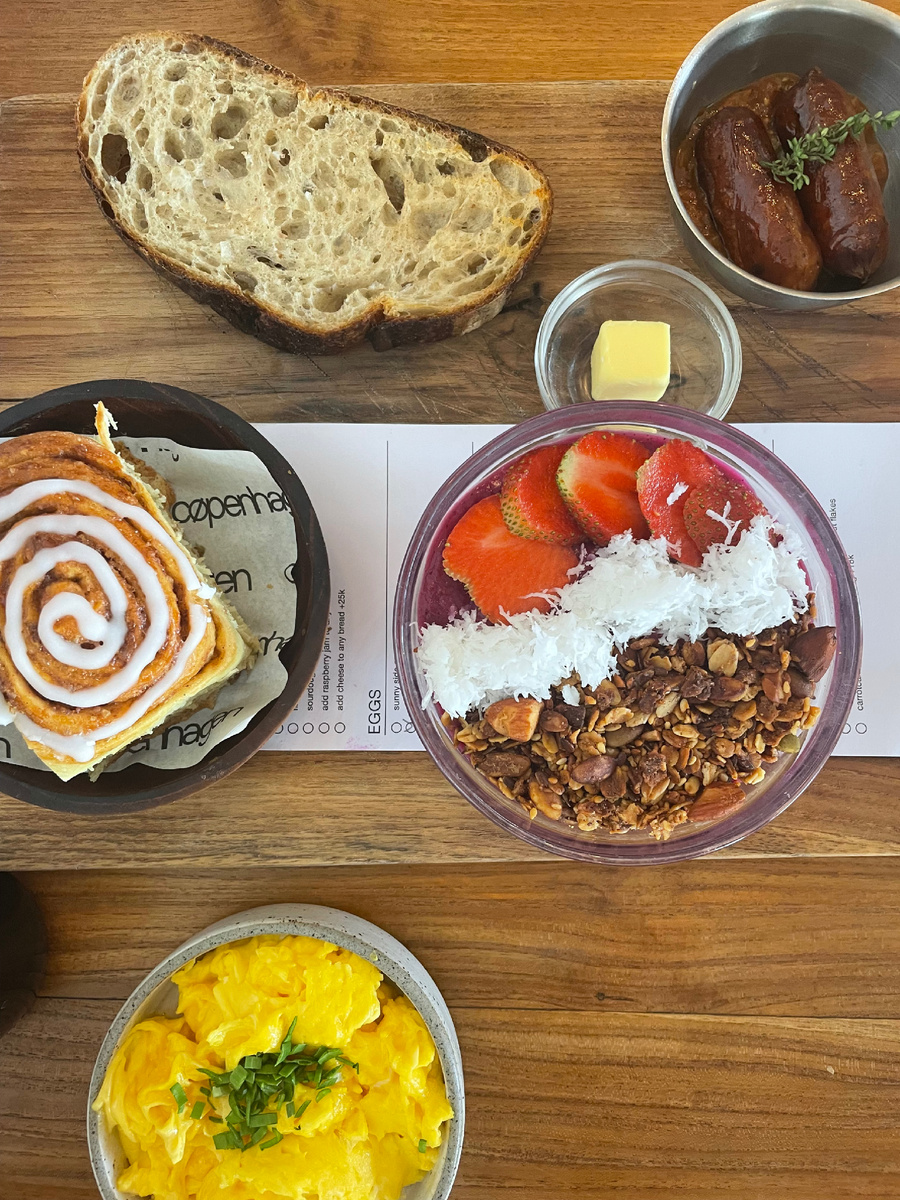 Завтрак из 5 позиций: скрэмбл, смузи-боул, булочка с корицей, куринные колбаски и злеб с соленым сливочным маслом.