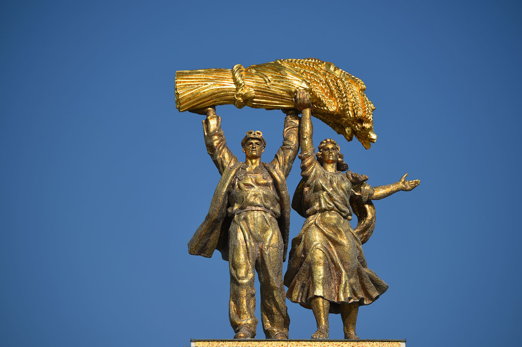 Фигура "Тракторист и колхозница". 1954. Скульптор Орлов С.М. При этом надо признать, что сама задумка не его - он только внёс изменения в  первоначальную композицию авторства Р. Н. Будилова и А.А. Стрекавина, установленную в 1939-м году. Правда, существенные. В первоначальном варианте тракторист поддерживает сноп только одной рукой, второй же вальяжно приобнимает колхозницу. В варианте 1954-го года эти вольности устранены - тракторист думает только о хлебе насущном и держит тяжёлый сноп двумя руками. Конечно, перекличка с "Рабочим и колхозницей" очевидна!  Фото взято из свободного доступа в интернете.