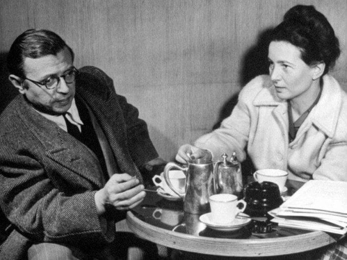 Симона де Бовуар справа. В белом пальто. Без очков. С её стороны ещё лежит папка с бумагами. А слева - Жань-Поль Сартр.