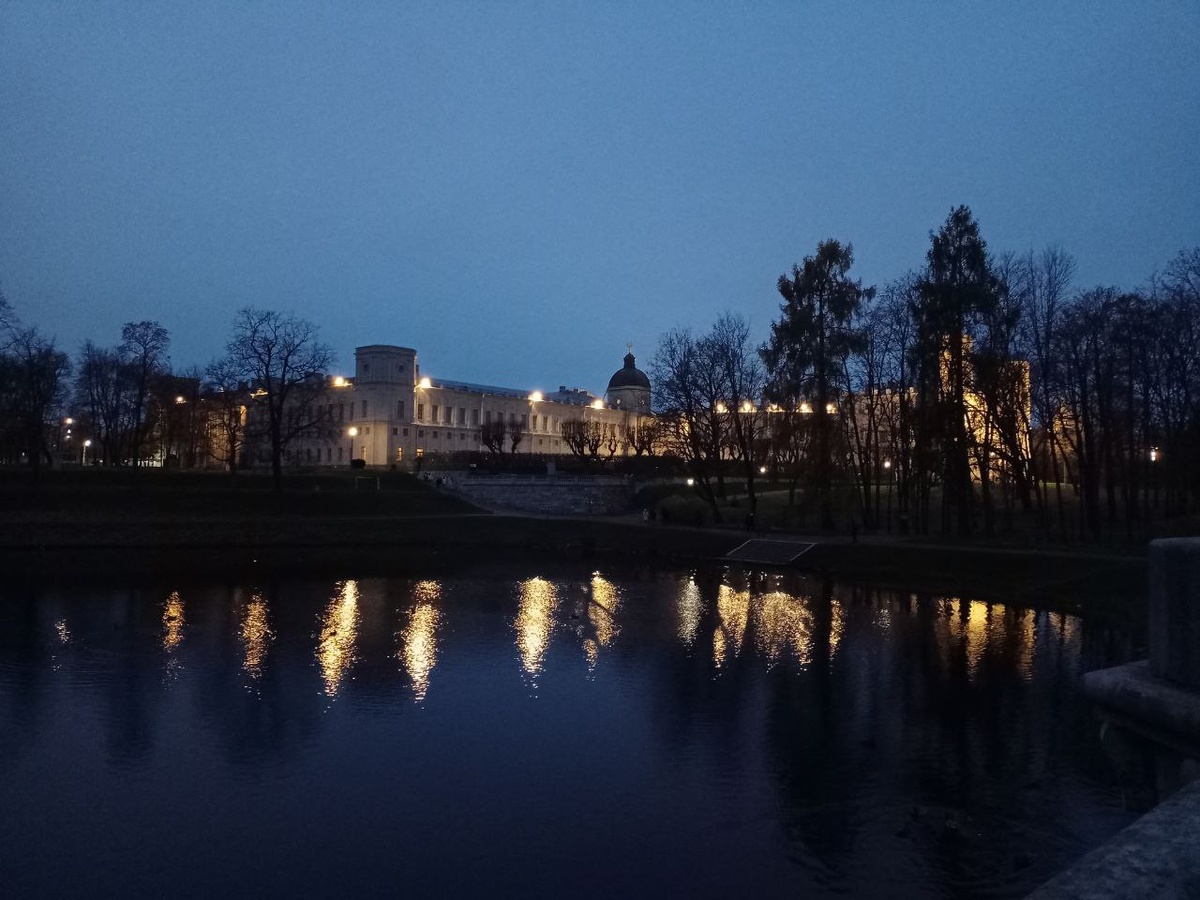 Панорама дворца. Глубокая осень, пасмурное небо и отблески фонарей в пруду, отражение которых нарушает лишь легкая рябь.