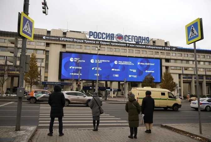 Пешеходы стоят на перекрёстке перед зданием международной медиагруппы «Россия сегодня» с бегущей строкой новостей о выборах в США, Москва, Россия, 6 ноября 2024 года. Павел Бедняков / AP.