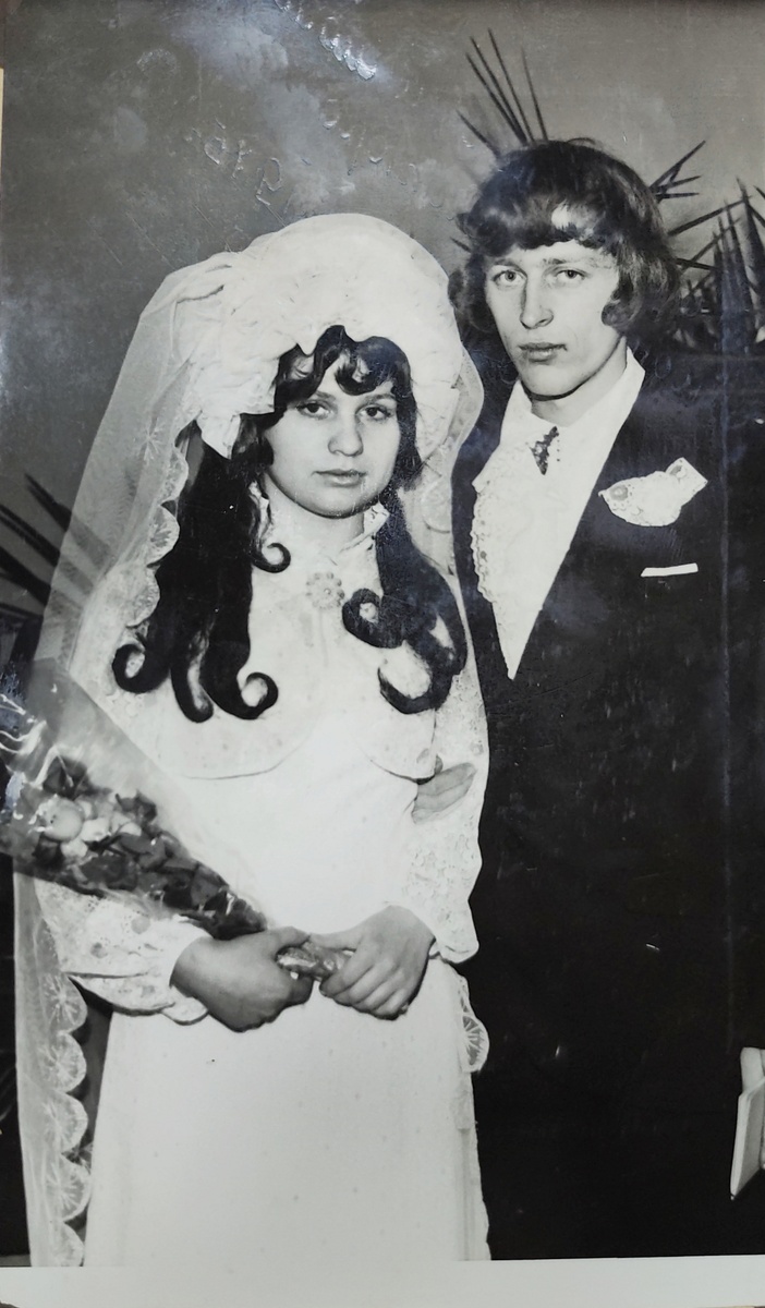 Тифлокомментарий. Фото 1975 года. Молодожёны. Молодая девушка с длинными чёрными волосами в свадебном платье и фате держит в руках цветы. И парень в костюме, в модной рубашке с кружевные жабо