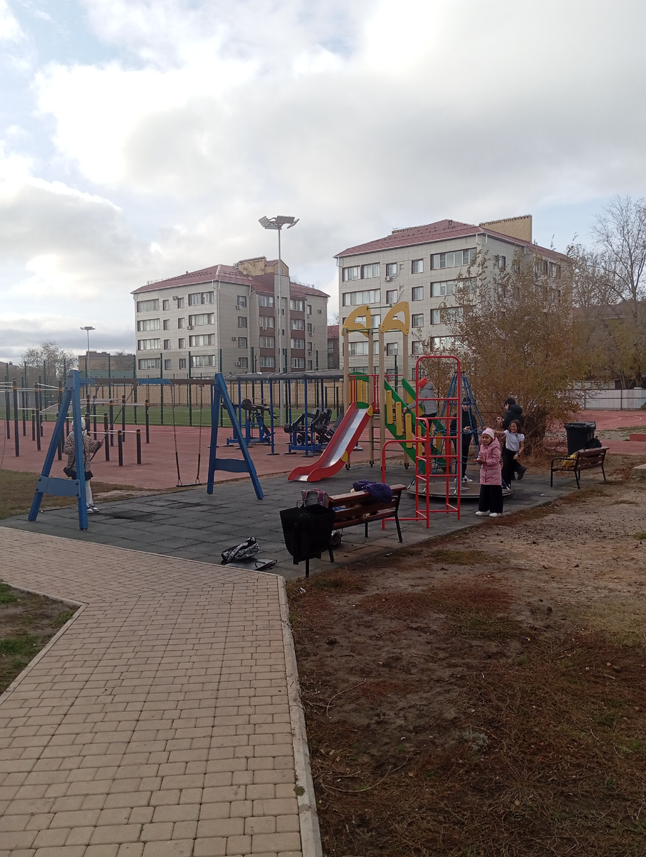 На школьной площадке девочка в летней блузке играет. 