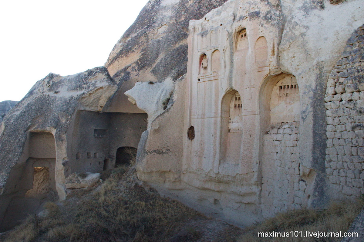 Скальный фасад усадьбы и провалившийся  внутренний двор. Слева виден кубический объем кухни с характерным  темными закопченными стенами, а также конусом дымохода. Как видим,  порталы построек сильно пострадали от скальной эрозии и обвалились.