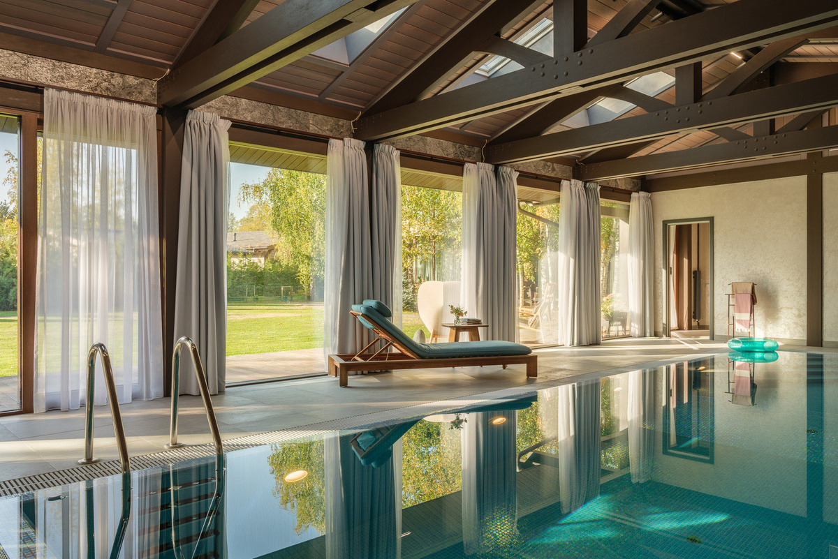 Панорамное остекление в бассейне позволяет любоваться видами из окон. А шторы создают уют и в вечернее время обеспечивают приватность
