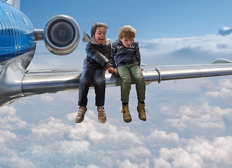 Два мальчика сидят на крыле самолета, летящего над облаками. Фото из Яндекса