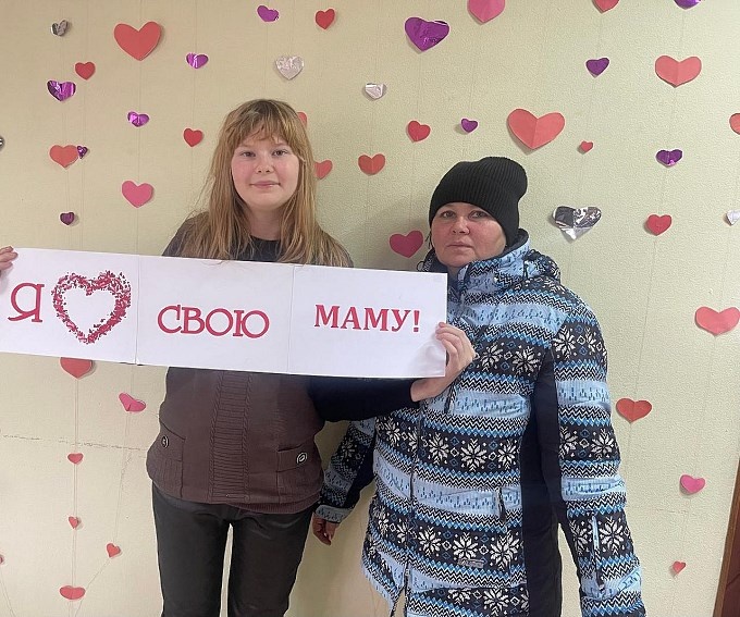 Дочь держит плакат «Я люблю свою маму»