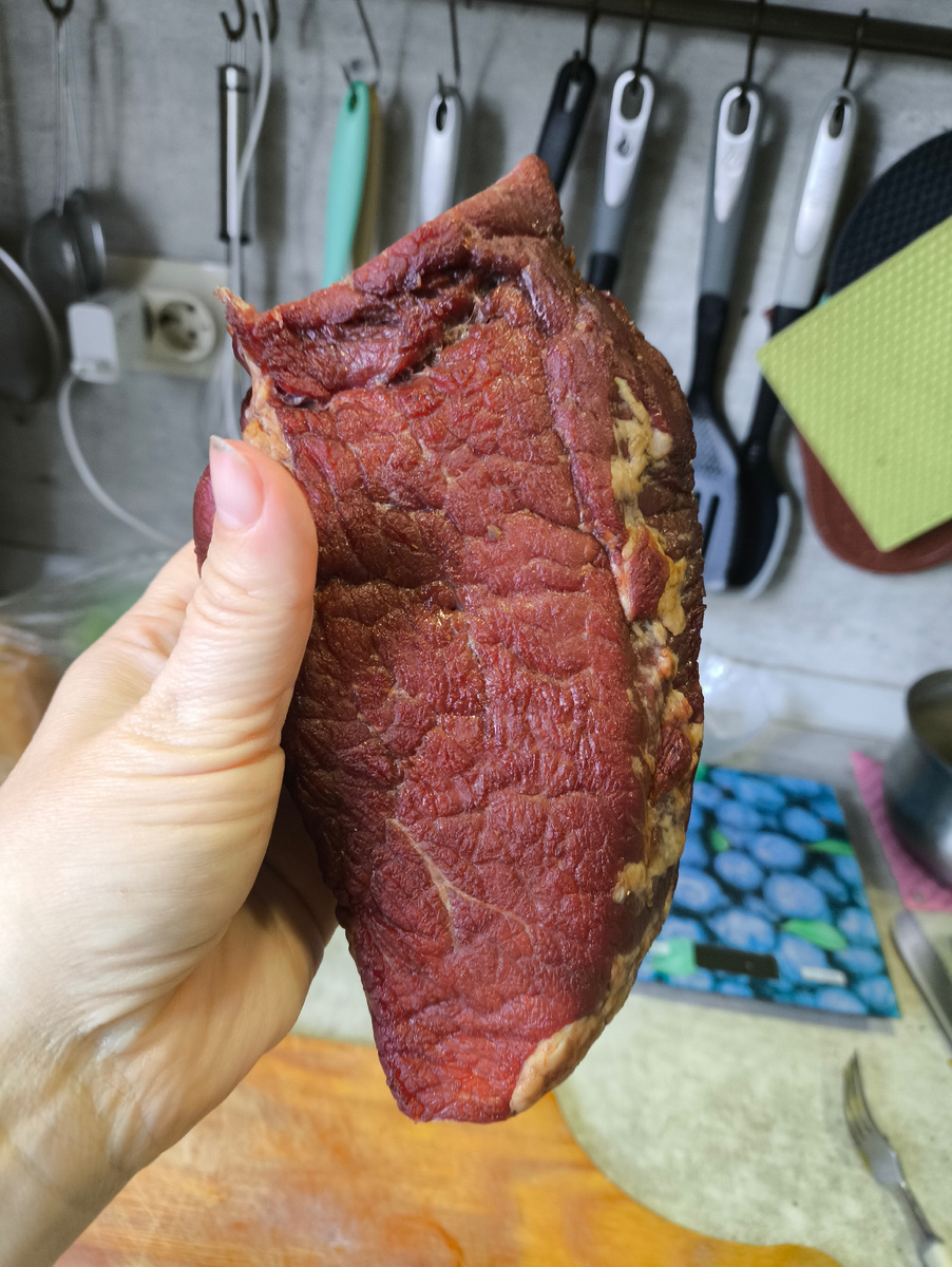 Тифлокомментарий. Женская рука держит кусок копчёной говядины. 