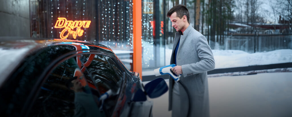    Автомобилист держит в руках зарядное устройство для электромобиля на АЗС сети «Газпромнефть»