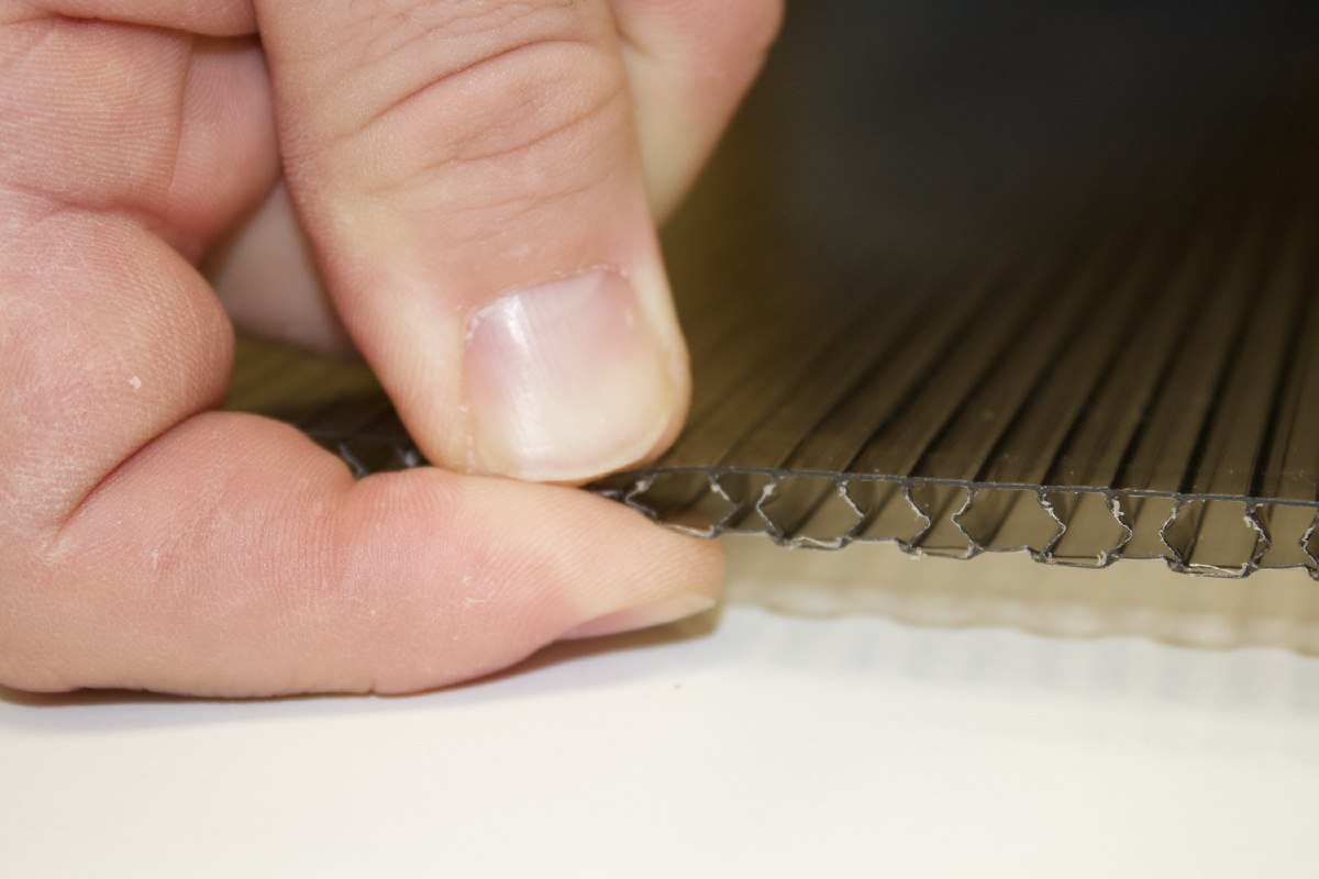 На фотографии показано как сжимать пальцами края листа поликарбоната. 