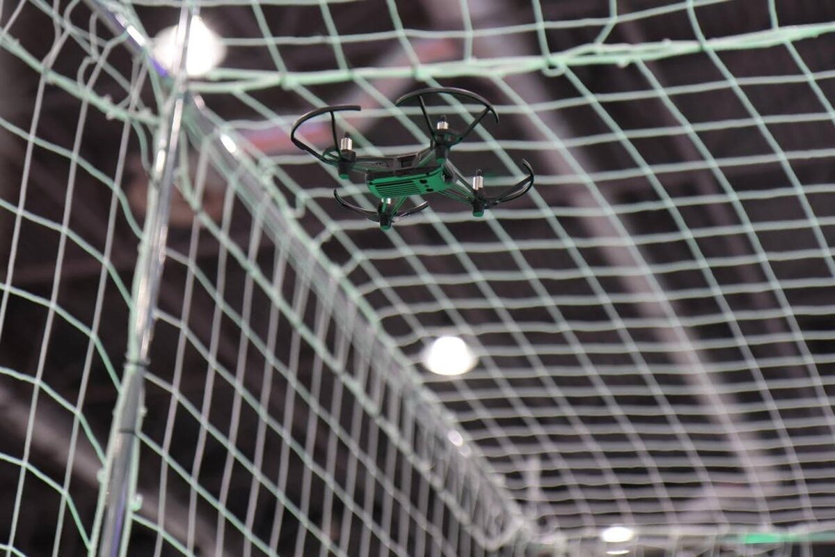 Управляемый дрон выполняет реальное полетное задание внутри специального сетчатого куба — огороженной со всех сторон прозрачной металлической сеткой клетки, размером 3 × 3 × 3 метра
