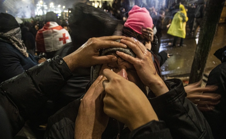 Демонстранты помогают друг другу спастись от слезоточивого газа, во время акции протеста возле парламента (Фото: Daro Sulakauri / Getty Images)