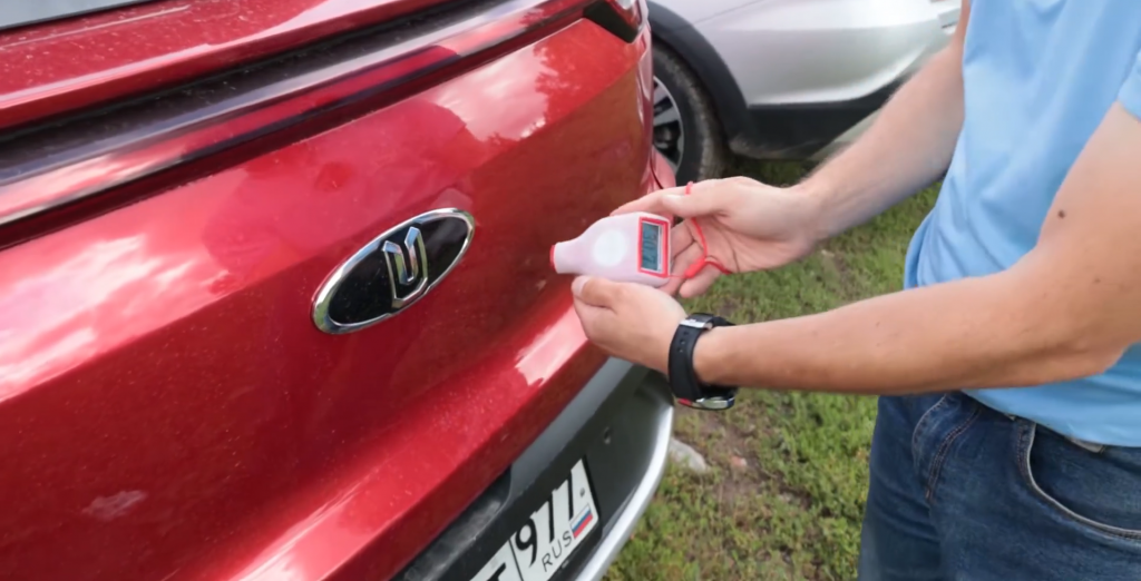 Ведущий AutoMPS Павел Кабанов замеряет толщину ЛКП на багажной двери кроссовера «Москвич 3» и активно ищет цинк.