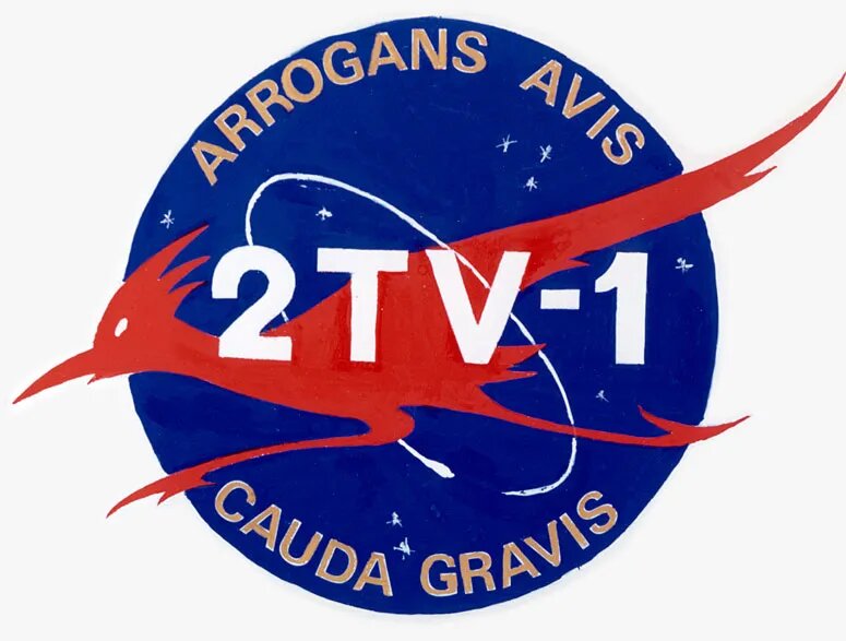 Логотипа термовакуумного испытания 2TV-1. Девиз гласит - «Arrogans Avis Cauda Gravis»: Гордая птица с тяжелым хвостом. Девиз был перефразированием слогана авиакомпании Continental Airlines «Гордая птица с золотым хвостом».
