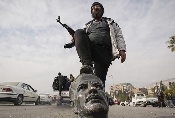    Сирийский повстанец у сломанного бюста бывшего президента Сирии Хафеза Аль-Асада