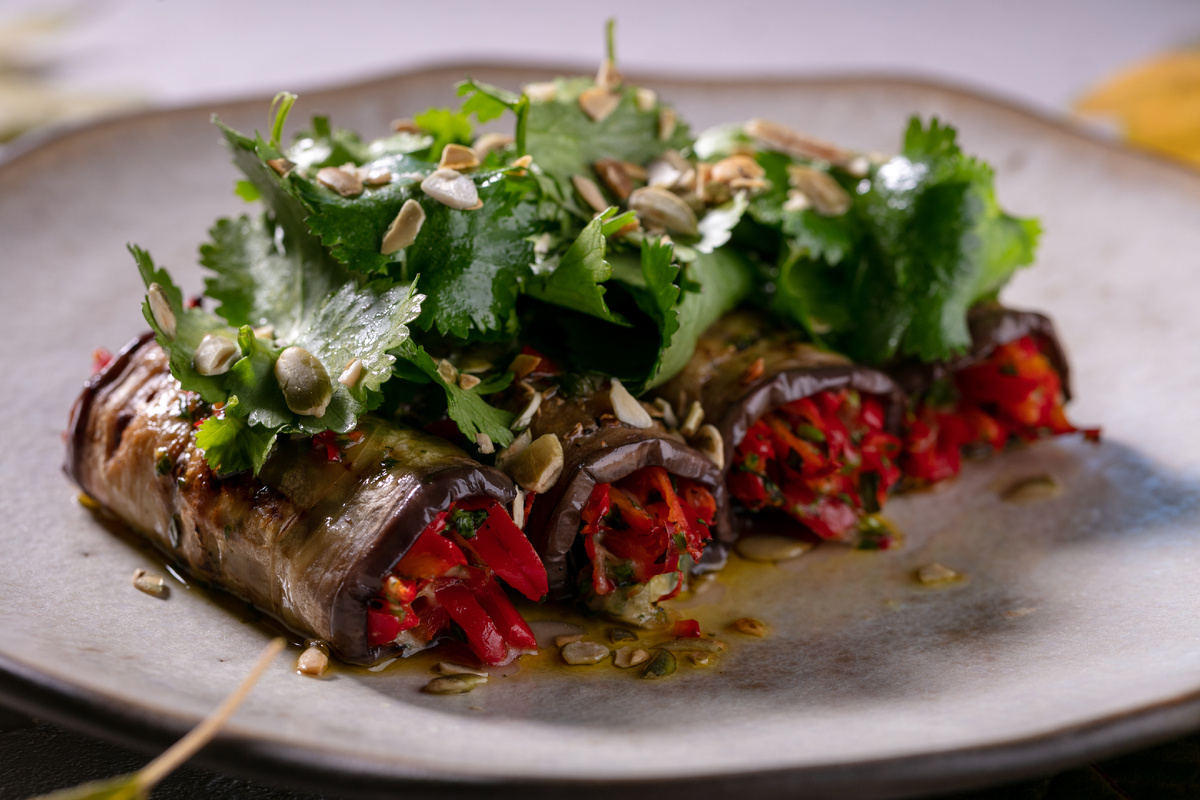 Слайсы из баклажанов, обжаренные на гриле и свёрнутые рулетом, с начинкой из сладкого перца и сыра «Качотта» с Фермы М2. Подаются со свежей зеленью и соусом «Чимичурри». 