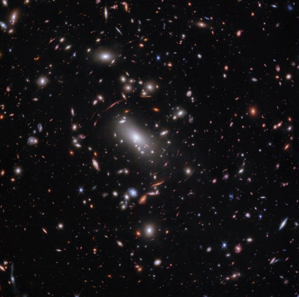    Thousands of glimmering galaxies are bound together by their own gravity, making up a massive cluster formally classified as MACS J1423. The largest bright white oval is a supergiant elliptical galaxy that is the dominant member of this galaxy cluster. The galaxy cluster acts like a lens, magnifying and distorting the light from objects that lie well behind it, an effect known as gravitational lensing that has big research benefits. Astronomers can study lensed galaxies in detail, like the Firefly Sparkle galaxy. This 2023 image is from the James Webb Space Telescope’s NIRCam (Near-InfraRed Camera). Researchers used Webb to survey the same field that the Hubble Space Telescope imaged in 2010. Thanks to its specialisation in high-resolution near-infrared imagery, Webb was able to show researchers many more galaxies in far more detail. [Image description: Thousands of overlapping objects at various distances are spread across this field, including galaxies in a massive galaxy cluster, and distorted background galaxies behind the galaxy cluster. The background of space is black.] Александр Шереметьев