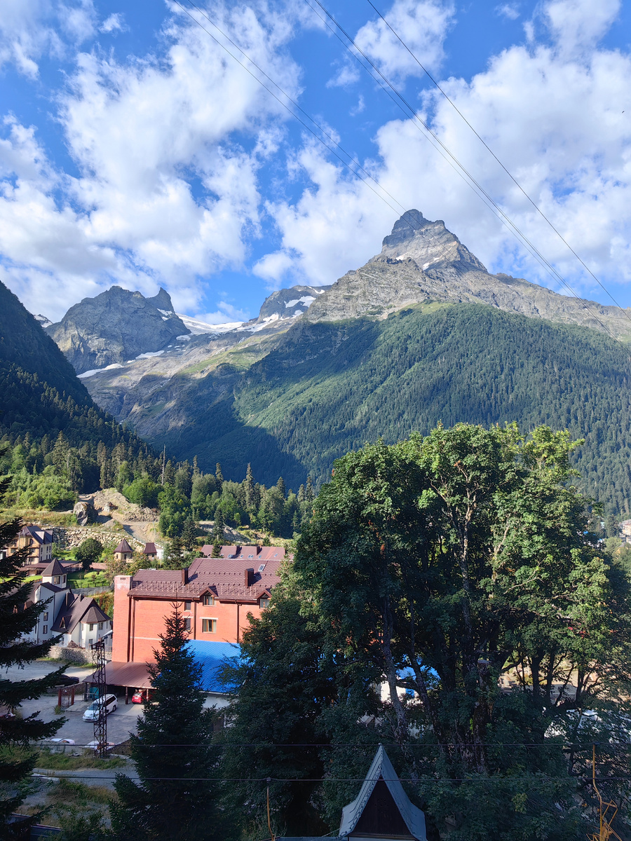 Посёлок Домбай, вид от гостиницы Наступ, рядом с местом посадки на старую кресельную канатку. Прямо по курсу-прекрасная Белалакая (в переводе с карачаево-балкарского "опоясанная светлым" или "полосатая скала"). В левой части фото - начало ущелья Аманауз,  вершина Суфруджу и ее характерной формы скальный выступ - Зуб Суфруджу (с балкарского переводится как "тигриный клык")