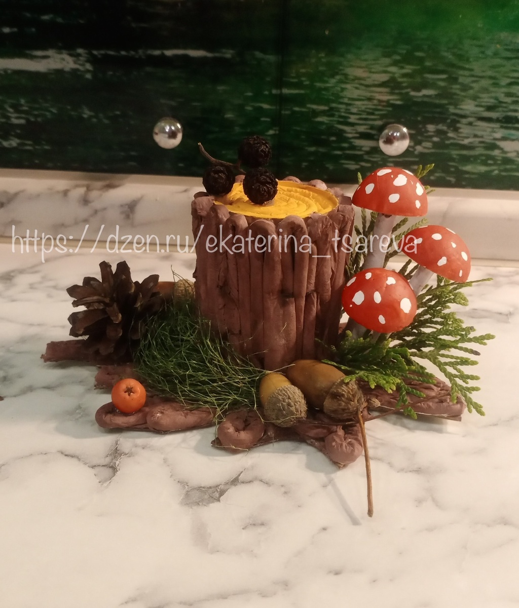 На картоне рисуем корни по кругу, в центр клеим втулку. Бумажные полотенца смачиваем из распылителя и скручиваем трубочки, высушиваем, клеим на картон, переходя на втулку, формируя кору. Во втулку вкладываем комки из газеты, из бумажной трубочки скручиваем улитку и клеим на верхушку втулки. Красим гуашью получившийся пенек. Пенопластовые шары режем пополам, раскрашиваем в мухоморы, ножки делаем из кусочков веток и красим в белый цвет. Клеим природные материалы. 