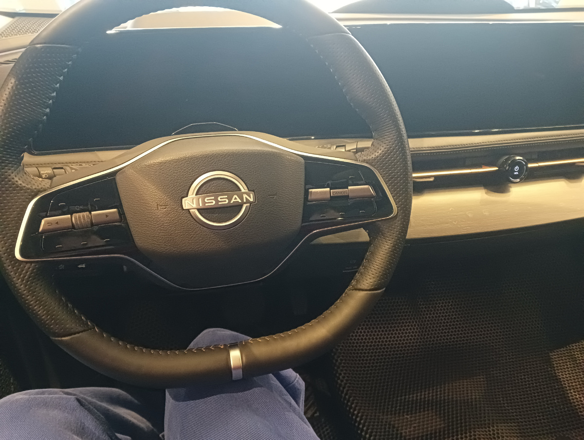 Приборная панель Nissan Ariya представляет собой вытянутый во всю ширину планшет, сверкающий чернотой при выключенном зажигании, а руль сделан двухспицевым