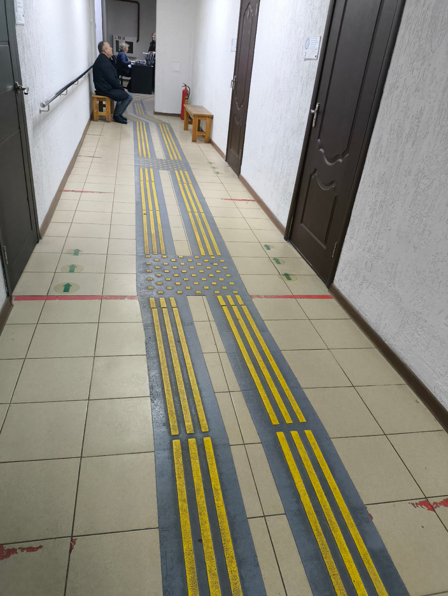 Тифлокомментарий. Коридор в соцзащите. Правильная тактильная плитка, скамейки, немногочисленные посетители