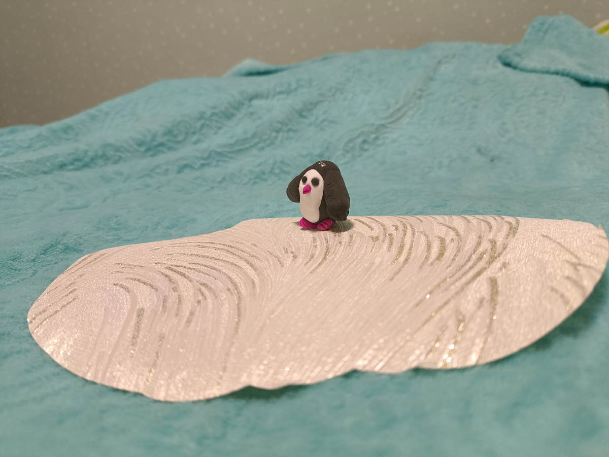 Тифлокомментарий. Голубой плед, на нём кусочек белых обоев. На нём маленький чёрный пингвин из воздушного пластилина. Если кто не понял, плед — это океан, обои — льдина, пингвин — Сёма. 