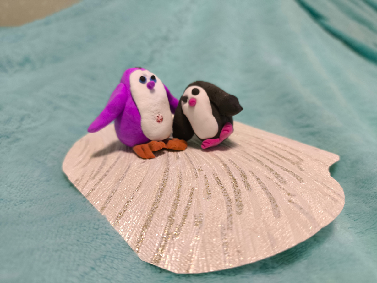 Тифлокомментарий. Мики и Сёма обнимаются. Мики — девочка, пластилиновый пингвин ярко-розового цвета. Сёма — мальчик. Он чёрный и намного меньше