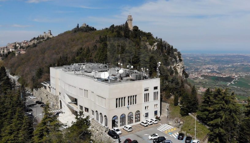 На фото: Штаб квартира San Marino RTV на виа Кеннеди, 13 (Via J.f. Kennedy, 13) в столице Республики Сан-Марино городе Сан-Марино (Città di San Marino). На заднем фоне мы видим башни крепостных сооружений Сан-Марино – в том числе (крупнее) башню Монтале, она же Третья башня (Montale -Terza Torre). Эти башни изображены на национальном флаге и гербе Сан-Марино.