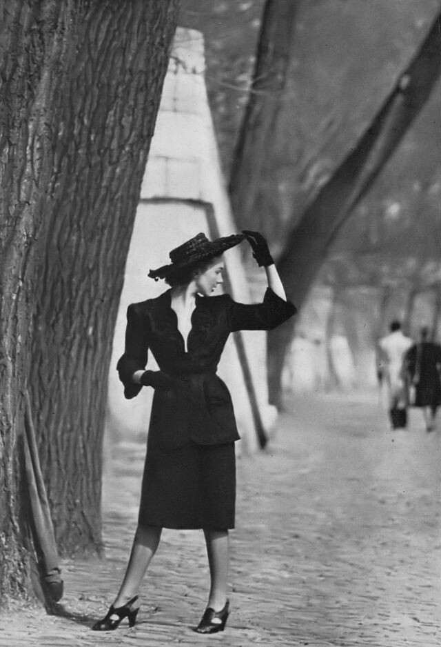 Модель в черном льняном костюме с глубоким волнистым вырезом и обильной черной вышивкой, пиджак плотно облегает талию, а затем округло приглаживается на бедрах, Роберт Пиге, фото Жана Мораля, Париж, Harper's Bazaar, июнь 1946 г.
