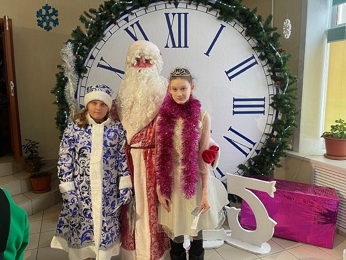 Девочка-подросток с Дедом Морозом и Снегурочкой на фоне больших часов