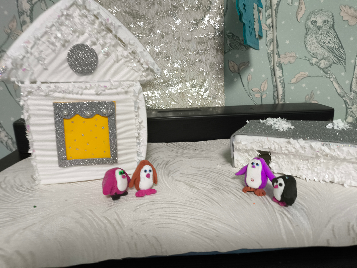 Тифлокомментарий. На куске белых обоев стоит домик, склееный из потолочный плит. У него жёлтое окно и серебристая отделка. Рядом прямоугольный пенопластовый домик с плоской серебристой крышей. Этот фон будет на всех фото. Четыре пингвина: Мики, Сёма, Марта и Марк. 