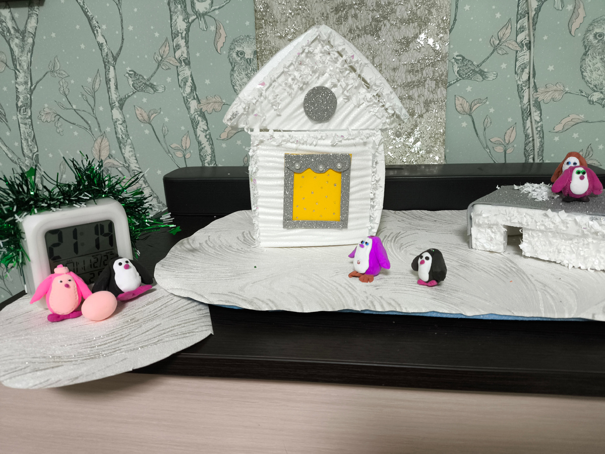 Тифлокомментарий. К большой льдине пристала маленькая, на ней два пингвина: розовый и чёрный. Перед ними большое яйцо, позади — квадратный белый будильник