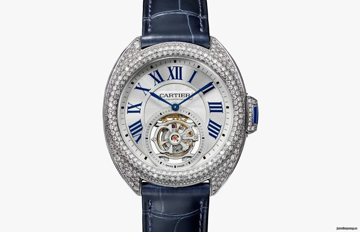 Женские часы Flying Tourbillon в стиле коллекции Clé de Cartier. Корпус из белого золота, усыпанный 478 бриллиантами, Квадратный сапфир на кнопке подзавода. Диаметр 35 мм