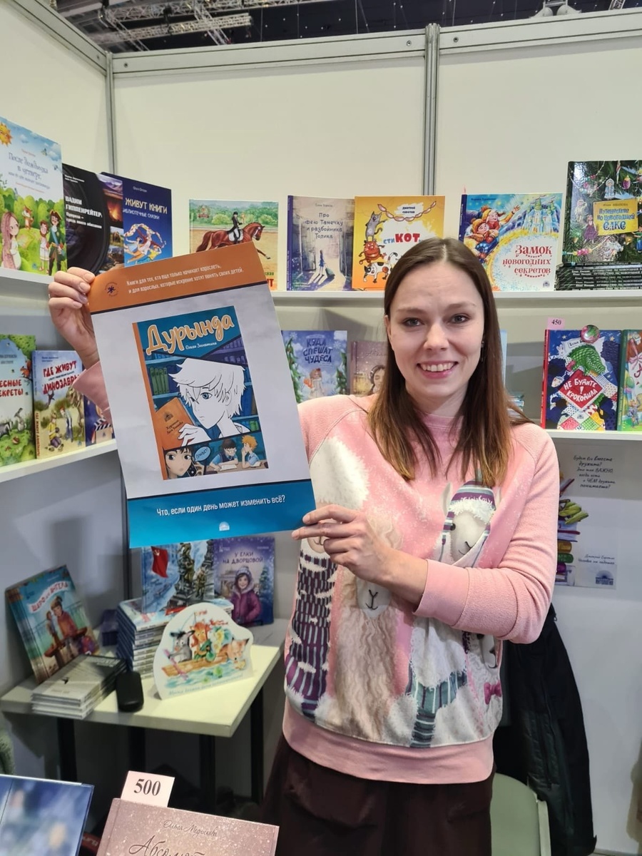 счастливый автор Ольга Замятина с плакатом обложки на Международной книжной ярмарке в Москве  (декабрь 2024 г.)