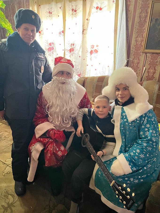 Мальчик с гитарой в окружении Деда Мороза и Снегурочки и сотрудника полиции