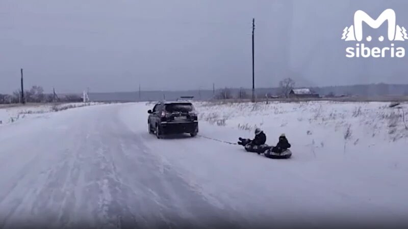     Дети катаются на тюбинге, привязанном к машине. Mash Siberia