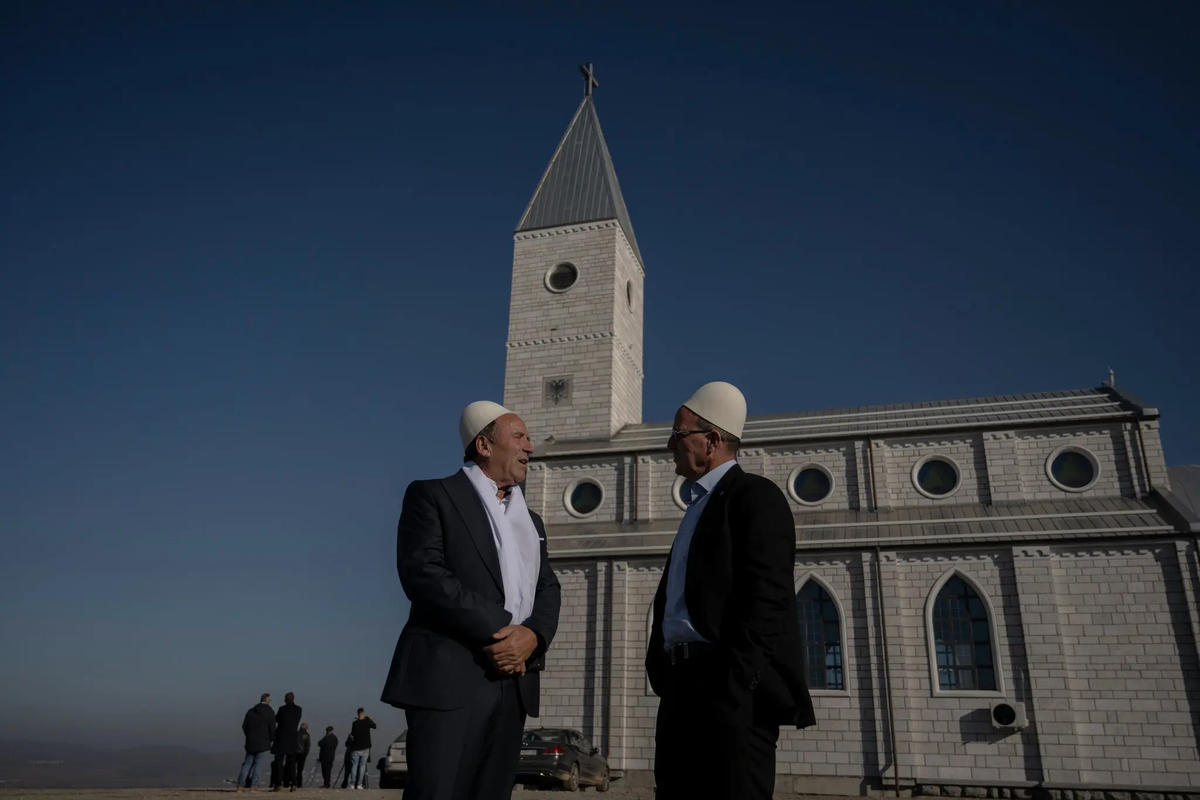 Двое мужчин беседуют перед церковью в деревне Ллапушник, Косово, где в ноябре состоялась церемония крещения. Фото Арменд Нимани для The New York Times.