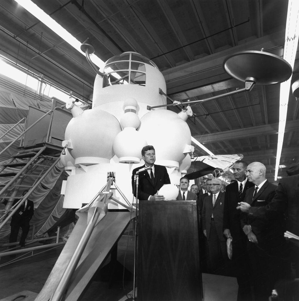 Президент США Джон Ф. Кеннеди в окружении вице-президента Линдона Бейнса Джонсона (справа) и представителей НАСА выступает перед сотрудниками Центра пилотируемых космических кораблей (MSC) в Хьюстоне, штат Техас, 12 сентября 1962 года. Макет лунного посадочного модуля "Аполлон" на этом фото является разработкой компании North American Aviation. (Фото НАСА)